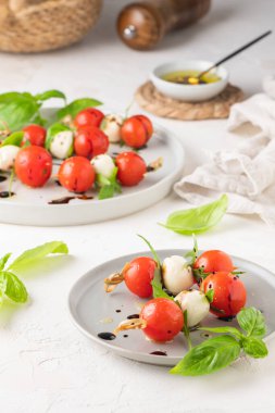 Domatesli şişler, mozarella topları, fesleğen ve baharatlar beyaz masada, yakın plan. İtalyan ev yapımı yemekler ve sağlıklı bir diyet konsepti..