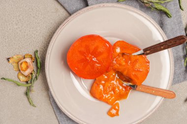 Hurma dilimleriyle taze olgun hurmalar tabakta çatal bıçaklar ve gri taşlı arka planda tüm meyveler. Mesaj için yer var. Yakın plan fotoğraf. Sağlık meyvesi kavramı.