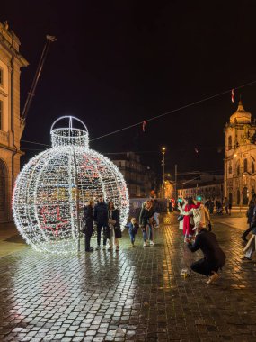 Porto, Portekiz - 9 Aralık 2023. Aslan çeşmesinin gece sahnesi. Yöre sakinleri ve ziyaretçiler Noel ışıklarını ve belediye binasının önündeki büyük Noel ağacını görmek için caddelerde yürüyorlar.