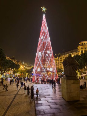 Porto, Portekiz - 9 Aralık 2023. Avenida dos Aliados ve Belediye Binası 'nın gece sahnesi Noel ağacıyla. Yöre sakinleri ve ziyaretçiler Noel ışıklarını ve belediye binasının önündeki büyük Noel ağacını görmek için caddelerde yürüyorlar.