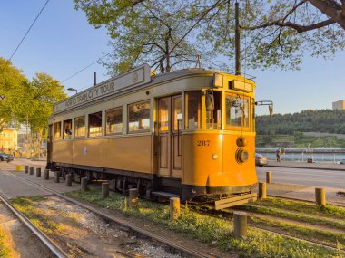 PORTO, PORTUGAL - 5 APRIL 2023: Tahta tarihi vintage sarı tramvay Porto caddesinde ilerliyor, şehrin sembolü. Günbatımında Arrabida Köprüsü ile Massarelos 'tan geçen eski tramvay. Yerliler ve intere için vazgeçilmez ulaşım