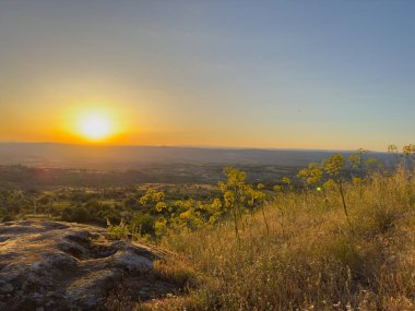 Golden sunset casting a warm glow over a serene village nestled among rocky hills and lush greenery. Linhares da Beira, Portugal clipart