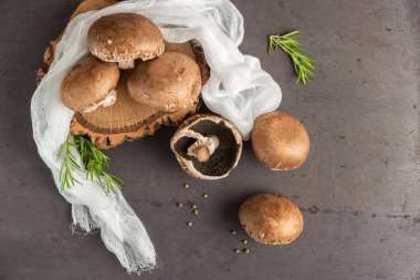 Beyaz bir bez ve biberiye filizi ile ahşap kesim tahtasındaki mantarlar