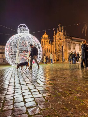 Porto, Portekiz - 9 Aralık 2023. Aslan çeşmesinin gece sahnesi. Yöre sakinleri ve ziyaretçiler Noel ışıklarını ve belediye binasının önündeki büyük Noel ağacını görmek için caddelerde yürüyorlar.