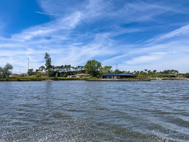 Parlak mavi bir gökyüzünün altında kıyıya vuran yumuşak su damlalarıyla sakin nehir manzarası. Bereketli yeşillik ve çevreyi çevreleyen ağaçlar huzur ve sükunet ortamını artırıyor. Ria de Aveiro 'daki Areinho plajı, Ovar - Portekiz.