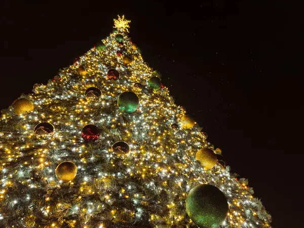 Yanıp sönen ışıklar ve renkli süslemelerle süslenmiş, yükselen bir Noel ağacı, neşeli ve büyülü bir atmosfer yaratır..