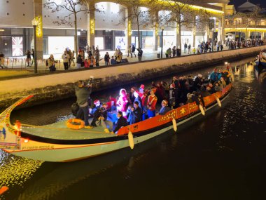 Aveiro, Portekiz - 01 Aralık 2023. Işıklarla süslenmiş ve neşeli yolcular taşıyan bir moliceiro teknesi Aveiro, Portekiz 'in aydınlık kanallarında dolaşarak büyülü bir Noel atmosferi yaratıyor..
