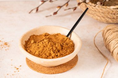 İnce zemin tarçın tozuyla dolu bej bir kase yuvarlak bir mantar altlığına yerleştirilir. Hassas söğüt dalları bulanık arkaplanda görünür..