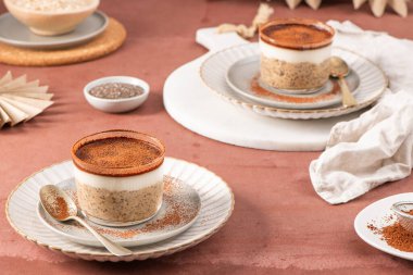 Üstü kremalı yoğurt ve kakao tozuyla kaplı Chia pudingi. Kırsal bir masada, zarif tabaklarda servis edilen cam kavanozlarda servis ediliyor.