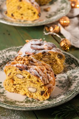 Yeşil çiçekli bir tabakta yeşil fındıklı ekmek diliminin yakın plan resmi. Üstünde şeker, badem, ceviz ve Noel süsleri olan yeşil bir masa. Bolo Rainha, Portekiz Noel tatlısı..