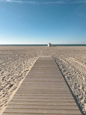 Uçsuz bucaksız kumlu bir sahil boyunca uzanan ahşap bir yol küçük beyaz bir kulübeye doğru uzanır, okyanus manzarası ve berrak mavi bir gökyüzü sunar. Figueira da Foz uzun ve güzel plajlarıyla tanınır, sakin yürüyüşleri ve kıyı şeridinin tadını çıkarması için mükemmeldir.
