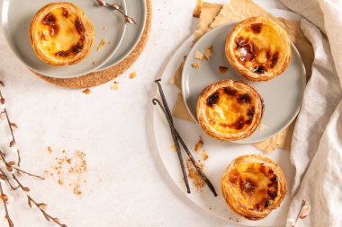 Geleneksel Portekiz kremalı tartları olan Pastel de Nata 'nın bir koleksiyonu vanilyalı fasulye ve söğüt dallarıyla birlikte tabaklar üzerinde düzenlenir. Üst görünüm