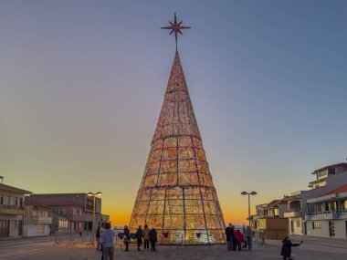 Cortegaca, Ovar, Portugal - december 24 2024. The largest crocheted Christmas tree in the world, 25 meters tall and with thousands of wool rosettes, stands illuminated at sunset. clipart