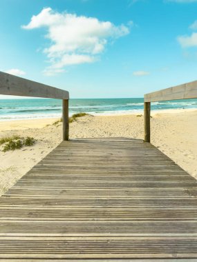 Tahta kaldırım, yumuşak dalgalar ve yumuşak beyaz bulutlarla kaplı açık mavi gökyüzü ile güneşli bir sahile çıkar. Huzurlu kıyı sahnesi Furadouro, Ovar, Portekiz 'de rahatlama ve tatil titreşimleri uyandırır.