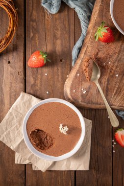 Bir kaşık dolusu zengin çikolatalı mus taze çilek ve narin beyaz çiçeklerle ahşap bir masada sunuluyor ve davetkar bir sahne yaratıyor.