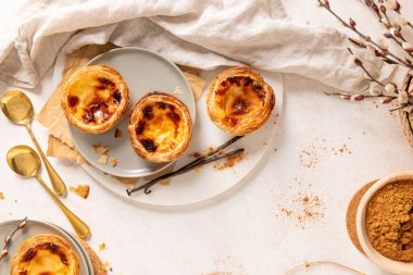 Geleneksel Portekiz kremalı tartları olan Pastel de Nata 'nın bir koleksiyonu vanilyalı fasulye ve söğüt dallarıyla birlikte tabaklar üzerinde düzenlenir. Üst görünüm