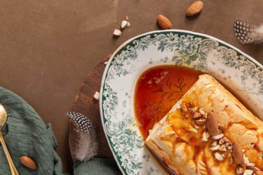 Hafifçe açılı bir yukarıdan çekimde, dekoratif bir tabakta servis edilen, bol bol şurup ve doğranmış bademle kaplı, Molotof ya da molotof olarak bilinen geleneksel karamelize edilmiş yumurta beyaz pudingi yer alır.