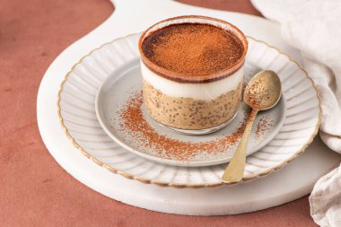 Chia pudingi, kremalı yoğurt ve kakao tozuyla birlikte beyaz bir tabakta altın kaşıkla servis edilir.