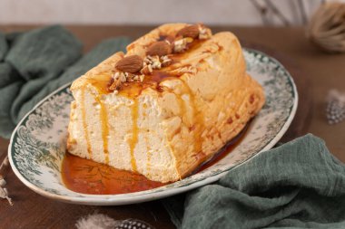 Hafif açılı yakın plan çekimde geleneksel karamelli yumurta beyaz pudingi Molotof ya da molotof olarak bilinen, bol karamelli ve bütün ve doğranmış bademlerle süslenmiş, dekoratif bir tabakta bulunur.