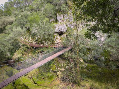 Yosunlu bir geçide yayılan asılmış yaya köprüsü, kireçtaşı uçurumlarından geçen yürüyüş yollarını birbirine bağlar, yemyeşil doğal ortamda ahşap kalaslar ve güvenlik kabloları bulunur. Rio de Mouros yolu, Condeixa, Coimbra Portekiz.