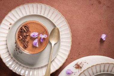 Genel bir bakış, bir bardakta kremalı çikolatalı mus yakalar, bir kaşık, çikolata talaşı ve mor çiçeklerle şekillendirilir..