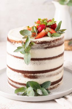 Taze çilekler ve okaliptüs filizi lezzetli, kırsal bir çikolatalı pastayı gri bir tabakta kremalı beyaz kremayla süsler..