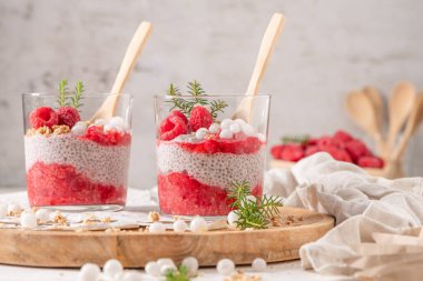 İki bardak katmanlı ahududu ve taze ahududu ve beyaz böğürtlenli chia tohumu pudingi kırsal ahşap tabakta servis edilir.