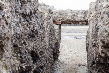 Yıpranmış beton bir yapı kayalık bir kıyı şeridinde kısmen bulutlu bir gökyüzünün altında sakin bir su kütlesinin altında duruyor. Bu da bir gizem ve tarih hissi uyandırıyor..