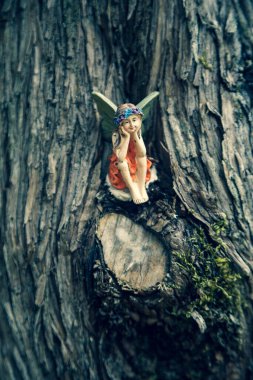 Ağaç gövdesine yaslanmış orman perisi figürü. Çocuklar için sihirli karakterler