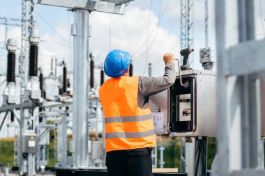 Koruyucu kasklı elektrikçi yüksek voltajlı elektrik hatları üzerinde çalışıyor. Elektrik şebekesine hizmet eden çok yetenekli işçiler. Güç kuleleri olan modern enerji santrali