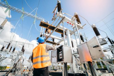 Koruyucu kasklı elektrikçi yüksek voltajlı elektrik hatları üzerinde çalışıyor. Elektrik şebekesine hizmet eden çok yetenekli işçiler. Güç kuleleri olan modern enerji santrali