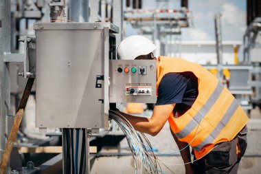 Koruyucu kasklı elektrikçi yüksek voltajlı elektrik hatları üzerinde çalışıyor. Elektrik şebekesine hizmet eden çok yetenekli işçiler. Güç kuleleri olan modern enerji santrali