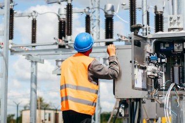 Koruyucu kasklı elektrikçi yüksek voltajlı elektrik hatları üzerinde çalışıyor. Elektrik şebekesine hizmet eden çok yetenekli işçiler. Güç kuleleri olan modern enerji santrali