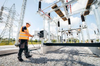 Koruyucu kasklı elektrikçi yüksek voltajlı elektrik hatları üzerinde çalışıyor. Elektrik şebekesine hizmet eden çok yetenekli işçiler. Güç kuleleri olan modern enerji santrali