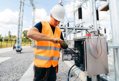 Koruyucu kasklı elektrikçi yüksek voltajlı elektrik hatları üzerinde çalışıyor. Elektrik şebekesine hizmet eden çok yetenekli işçiler. Güç kuleleri olan modern enerji santrali