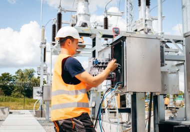 Koruyucu kasklı elektrikçi yüksek voltajlı elektrik hatları üzerinde çalışıyor. Elektrik şebekesine hizmet eden çok yetenekli işçiler. Güç kuleleri olan modern enerji santrali