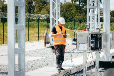 Koruyucu kasklı elektrikçi yüksek voltajlı elektrik hatları üzerinde çalışıyor. Elektrik şebekesine hizmet eden çok yetenekli işçiler. Güç kuleleri olan modern enerji santrali