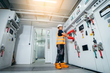 Erişkin elektrikçi mühendisi sigorta kutusunda test ve vida ekipmanı ve tabletteki verileri kullanarak modern elektrik santralinin onarımını otomatik kontrol dolabı.