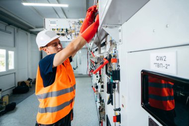 Adult electrician builder engineer testing and screwing equipment in fuse box and repairing of modern electricity power station using data from the tablet.. Automatic control cabinet clipart