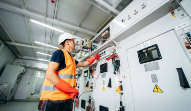 Erişkin elektrikçi mühendisi sigorta kutusunda test ve vida ekipmanı ve tabletteki verileri kullanarak modern elektrik santralinin onarımını otomatik kontrol dolabı.