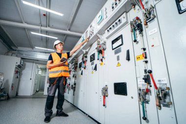 Erişkin elektrikçi mühendisi sigorta kutusunda test ve vida ekipmanı ve tabletteki verileri kullanarak modern elektrik santralinin onarımını otomatik kontrol dolabı.