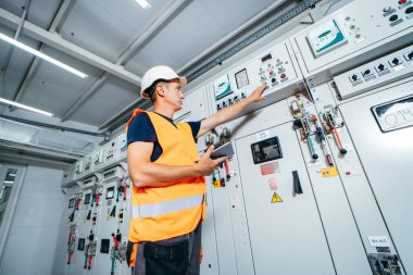 Erişkin elektrikçi mühendisi sigorta kutusunda test ve vida ekipmanı ve tabletteki verileri kullanarak modern elektrik santralinin onarımını otomatik kontrol dolabı.