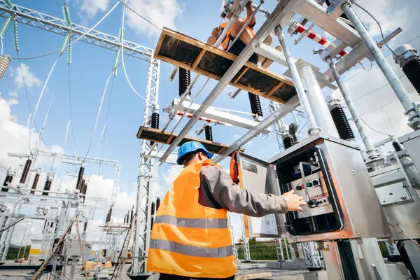 Koruyucu kasklı elektrikçi yüksek voltajlı elektrik hatları üzerinde çalışıyor. Elektrik şebekesine hizmet eden çok yetenekli işçiler. Güç kuleleri olan modern enerji santrali