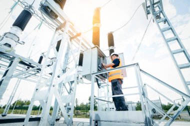 Koruyucu kasklı elektrikçi yüksek voltajlı elektrik hatları üzerinde çalışıyor. Elektrik şebekesine hizmet eden çok yetenekli işçiler. Güç kuleleri olan modern enerji santrali