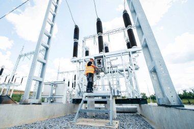 Koruyucu kasklı elektrikçi yüksek voltajlı elektrik hatları üzerinde çalışıyor. Elektrik şebekesine hizmet eden çok yetenekli işçiler. Güç kuleleri olan modern enerji santrali