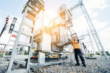 Koruyucu kasklı elektrikçi yüksek voltajlı elektrik hatları üzerinde çalışıyor. Elektrik şebekesine hizmet eden çok yetenekli işçiler. Güç kuleleri olan modern enerji santrali