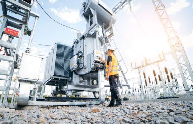 Koruyucu kasklı elektrikçi yüksek voltajlı elektrik hatları üzerinde çalışıyor. Elektrik şebekesine hizmet eden çok yetenekli işçiler. Güç kuleleri olan modern enerji santrali
