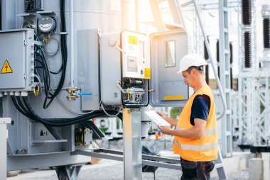 Koruyucu kasklı elektrikçi yüksek voltajlı elektrik hatları üzerinde çalışıyor. Elektrik şebekesine hizmet eden çok yetenekli işçiler. Güç kuleleri olan modern enerji santrali