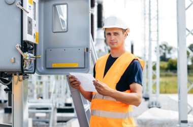Koruyucu kasklı elektrikçi yüksek voltajlı elektrik hatları üzerinde çalışıyor. Elektrik şebekesine hizmet eden çok yetenekli işçiler. Güç kuleleri olan modern enerji santrali