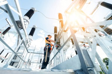 Koruyucu kasklı elektrikçi yüksek voltajlı elektrik hatları üzerinde çalışıyor. Elektrik şebekesine hizmet eden çok yetenekli işçiler. Güç kuleleri olan modern enerji santrali